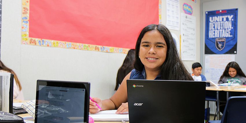 middle school girl smiling with laptop in front of her