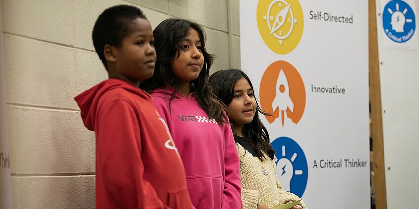 three students standing beside a sign showing competencies for graduates