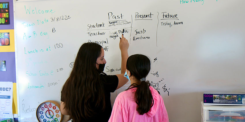 two girls writing on a whiteboard on a design challenge