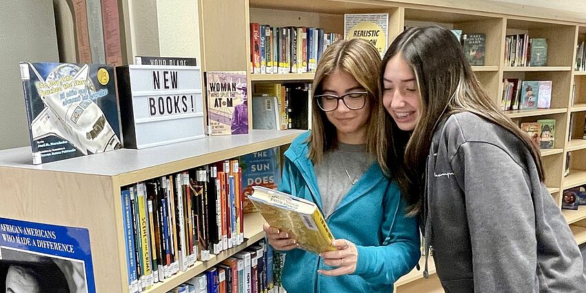 two female students in the library looking at book together