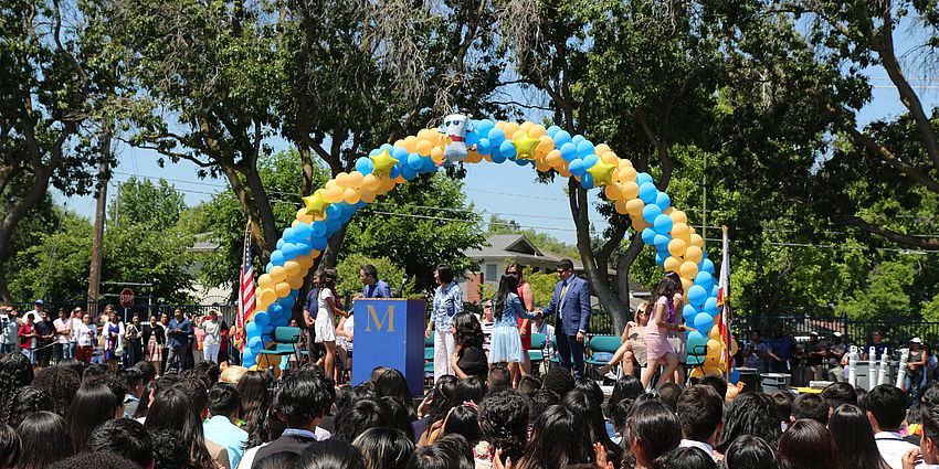 Arch of balloons above the stage where students are crossing for a promotional ceremony 
