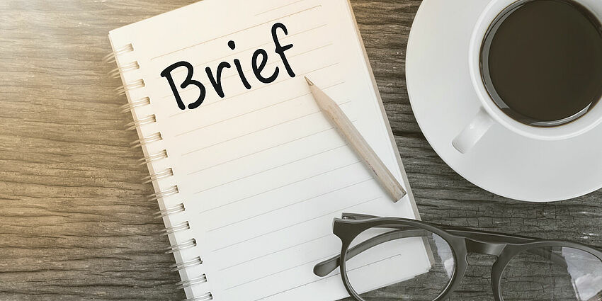 cup of coffee and notebook with brief written and a set of glasses 