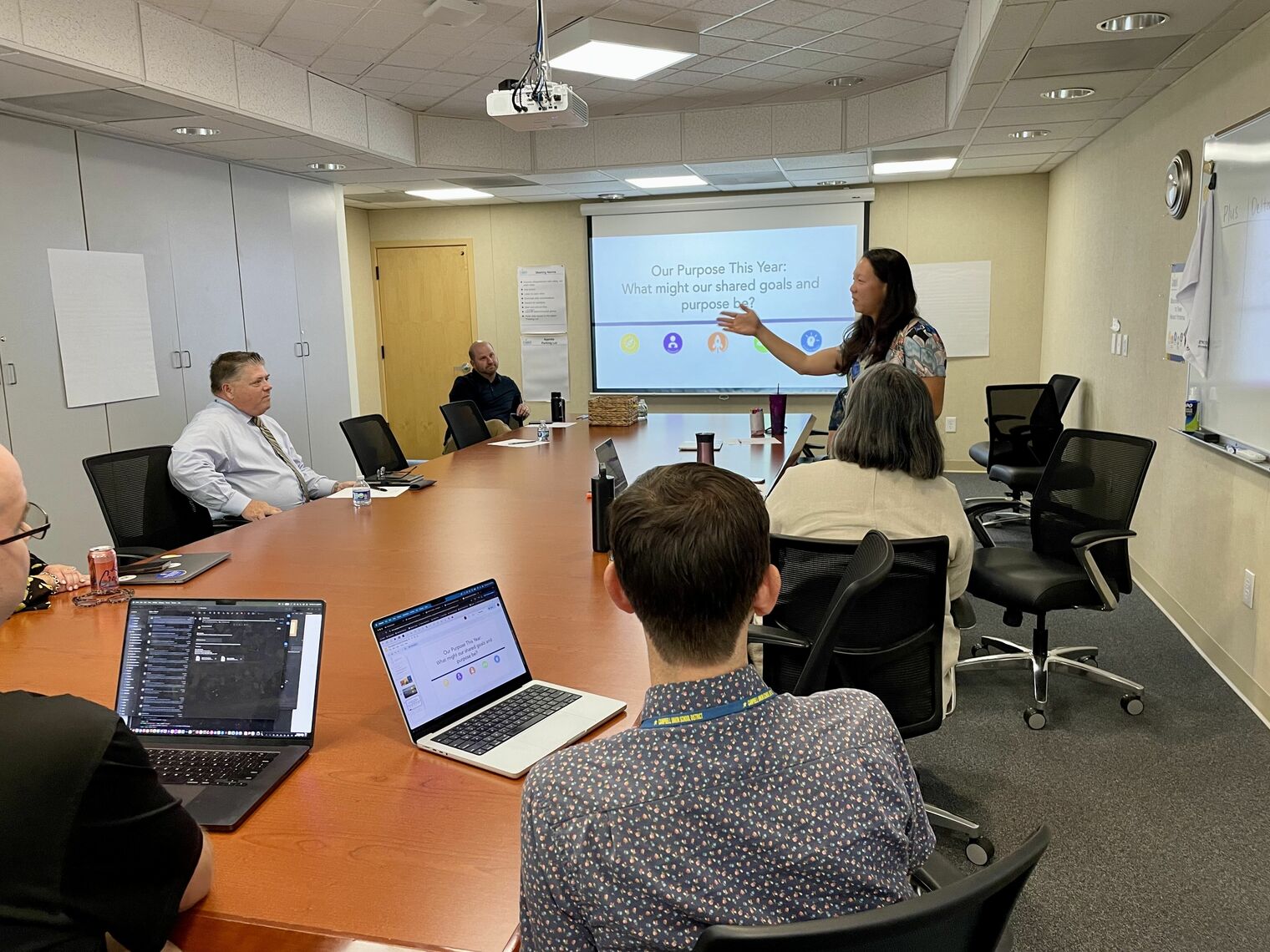 woman stands and talks to group of people seated at a conference table