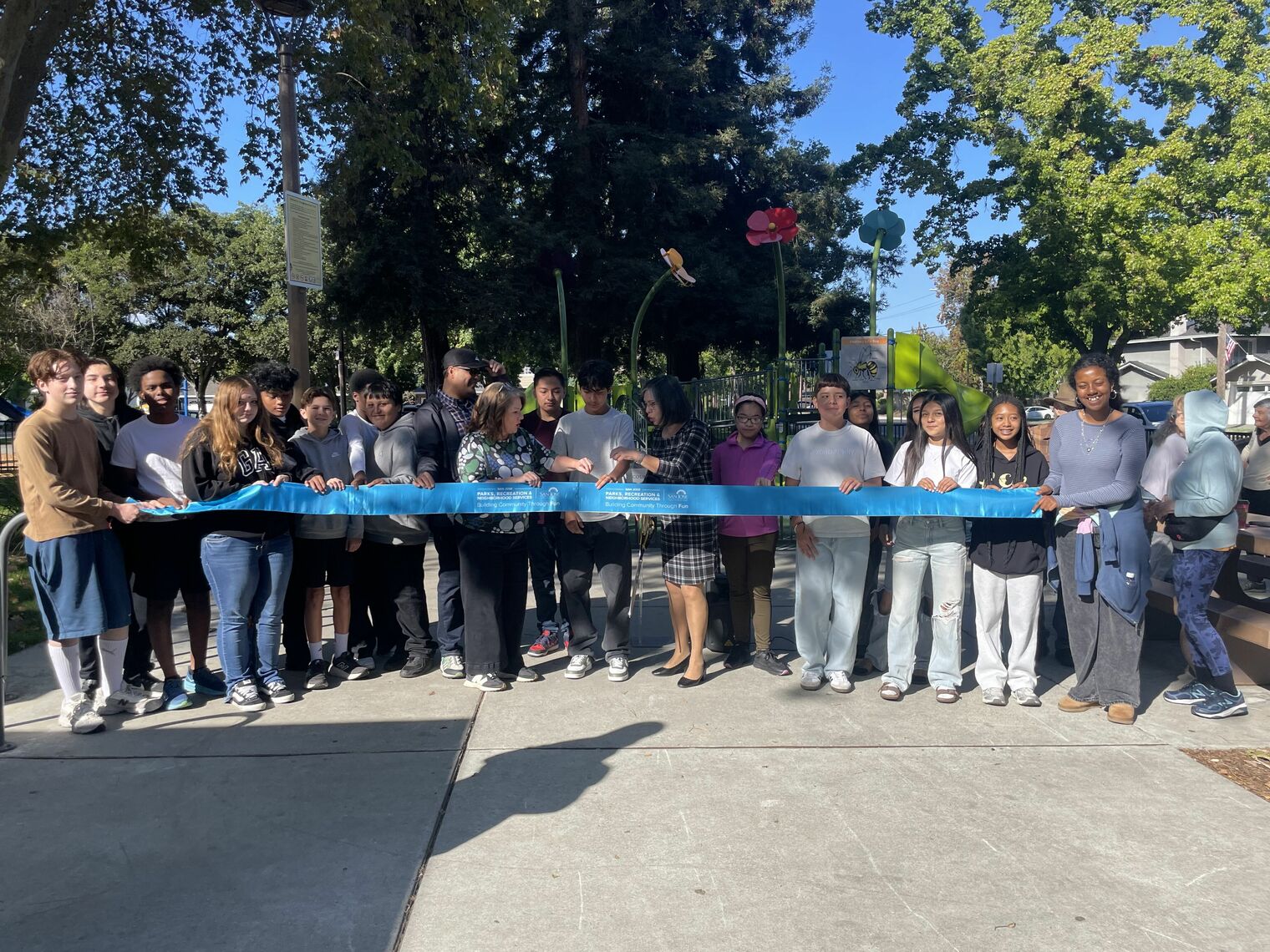 students standing behind the blue ribbon being cut in the park