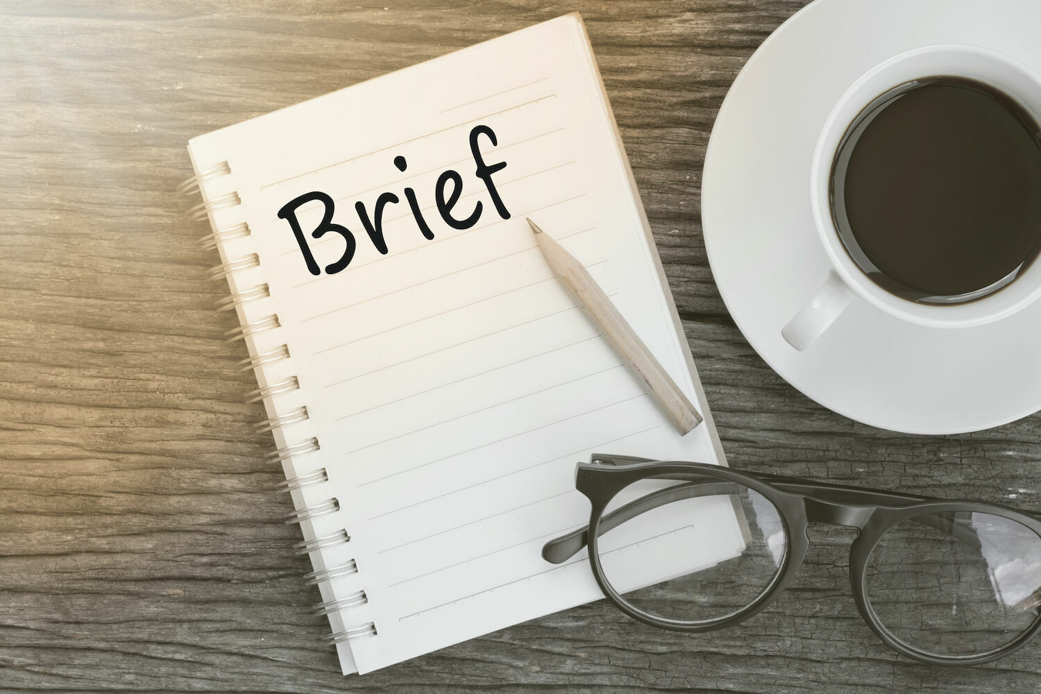 cup of coffee and notebook with brief written and a set of glasses 